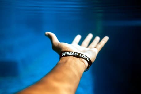  a hand reaching out with a wristband that says spread love.