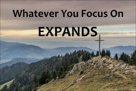 view of the mountains with a cross on top of it and the words: whatever you focus on expands